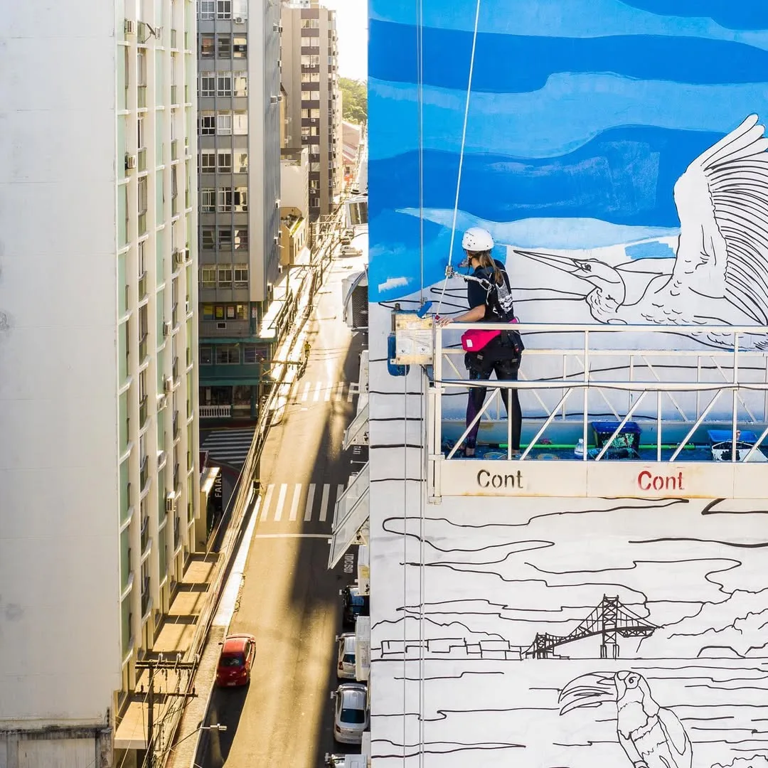 Tuane Arte pintando mural em prédio com andaime suspenso em Florianópolis
